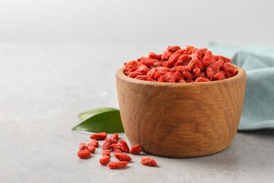 Dried goji berries in bowl and green leaves on light grey table, space for text