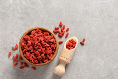 Dried goji berries in bowl and scoop on light grey table, top view. Space for text