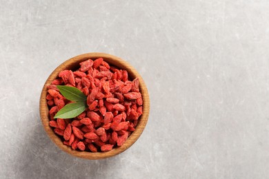 Photo of Dried goji berries in bowl and green leaves on light grey table, top view. Space for text