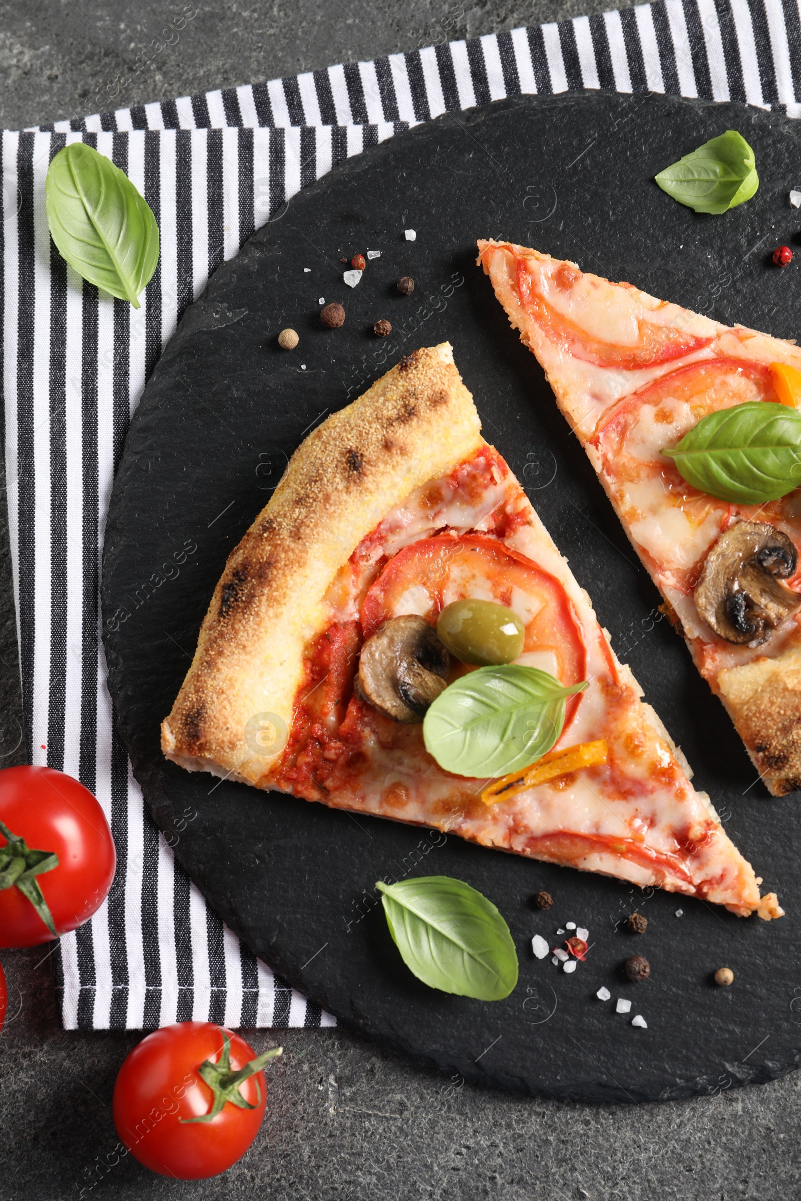 Photo of Cut delicious vegetarian pizza, spices and tomatoes on grey table, top view