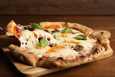 Photo of Taking piece of delicious vegetarian pizza at wooden table, closeup