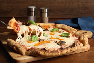 Photo of Taking piece of delicious vegetarian pizza at wooden table, closeup