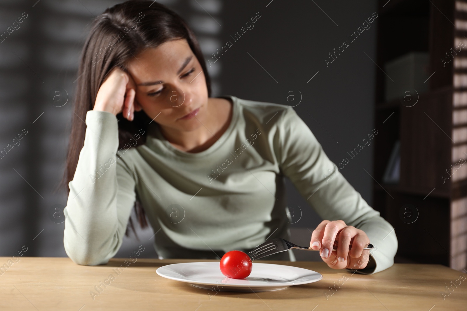 Photo of Eating disorder. Sad woman with fork near tomato at wooden table