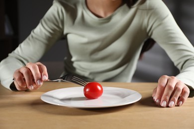 Photo of Eating disorder. Woman with fork near tomato at wooden table, closeup