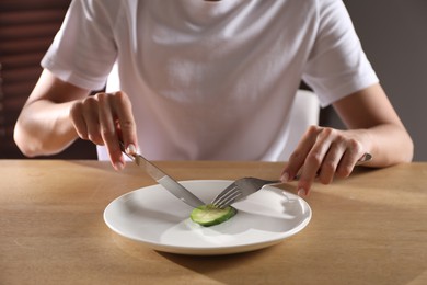 Eating disorder. Woman cutting cucumber at wooden table indoors, closeup