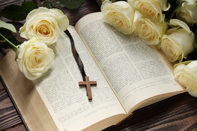 Bible, cross and roses on wooden table, closeup. Religion of Christianity