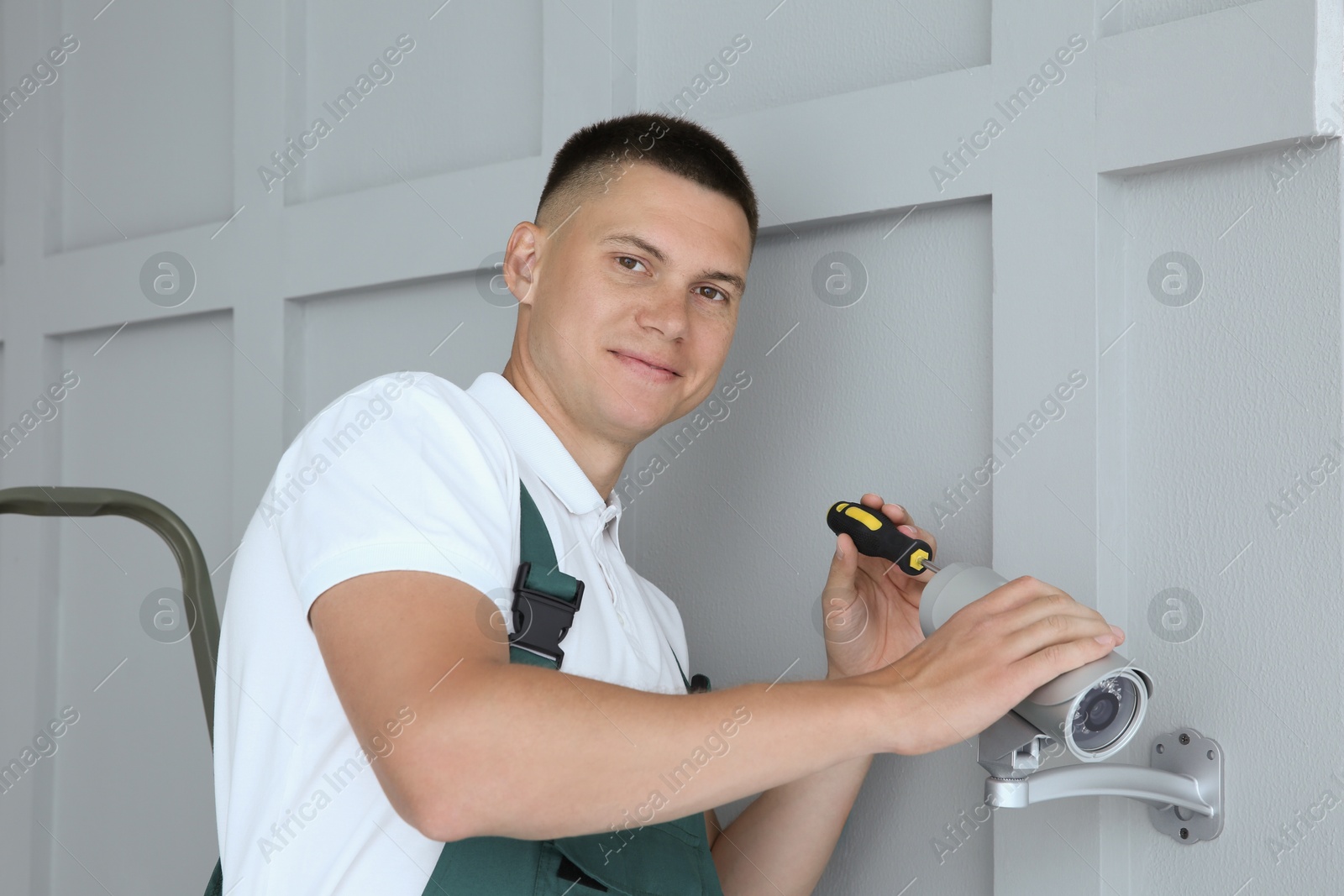 Photo of Technician with screwdriver installing CCTV camera on wall indoors