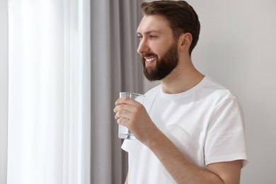 Happy young man with glass of water near window at morning
