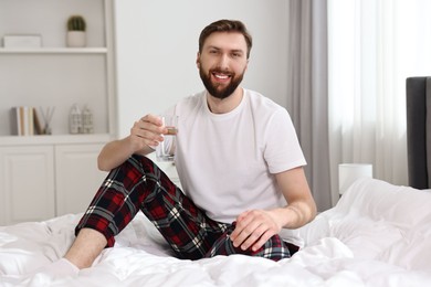 Happy young man with glass of water near on bed at morning