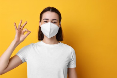 Woman in respirator mask showing OK gesture on orange background, space for text