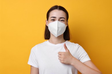 Photo of Woman in respirator mask showing thumbs up on orange background