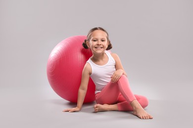 Photo of Cute little girl with fit ball on grey background