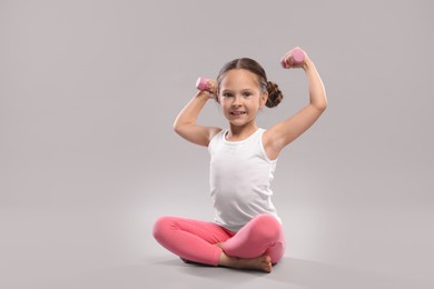Cute little girl with dumbbells on grey background, space for text