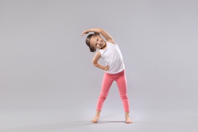 Cute little girl stretching on grey background