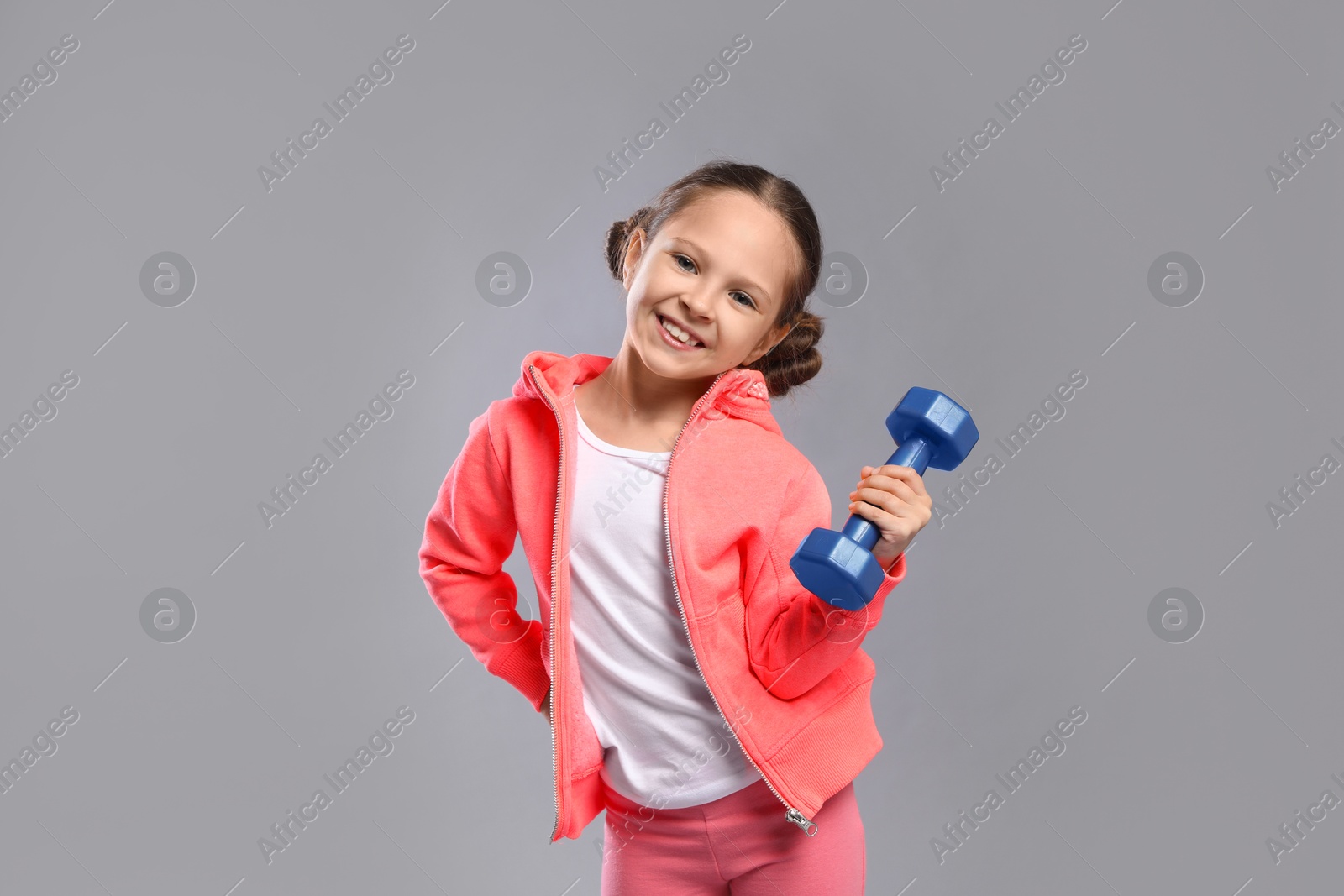 Photo of Cute little girl with dumbbell on grey background