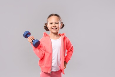 Photo of Cute little girl with dumbbell on grey background