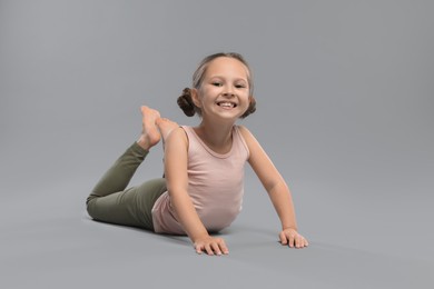 Cute little girl stretching on grey background