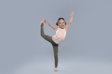 Cute little girl stretching on grey background