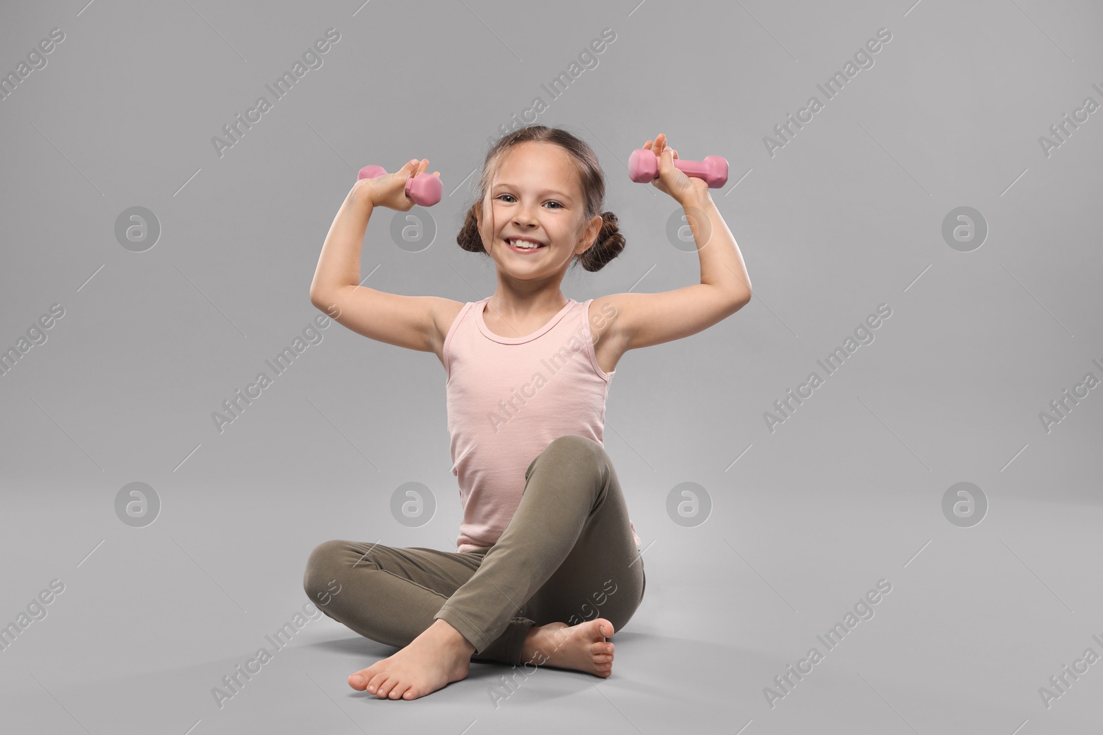 Photo of Cute little girl with dumbbells on grey background