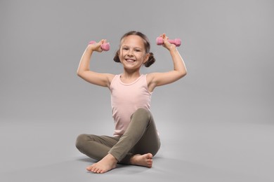 Cute little girl with dumbbells on grey background