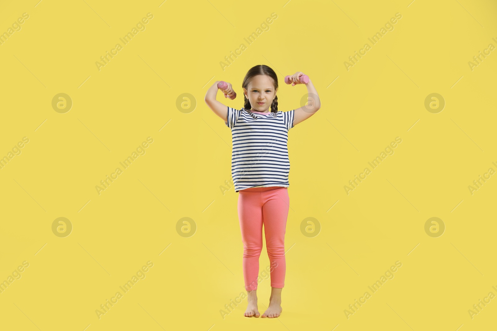 Photo of Cute little girl with dumbbells on yellow background