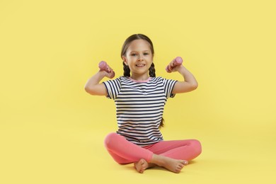 Photo of Cute little girl with dumbbells on yellow background