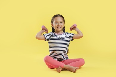 Cute little girl with dumbbells on yellow background