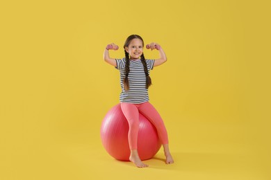 Photo of Cute little girl with dumbbells and fit ball on yellow background