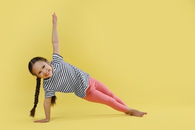 Photo of Cute little girl doing gymnastic exercise on yellow background, space for text