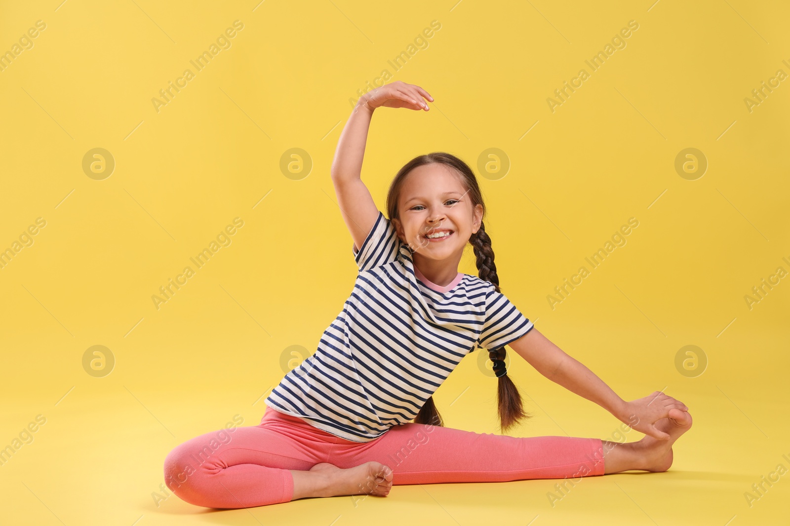 Photo of Cute little girl stretching on yellow background