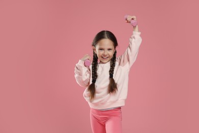 Cute little girl with dumbbells on pink background