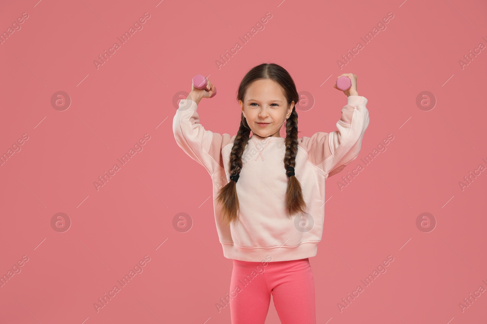 Photo of Cute little girl with dumbbells on pink background