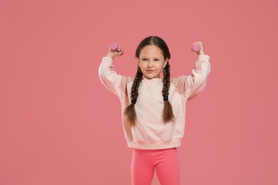 Cute little girl with dumbbells on pink background