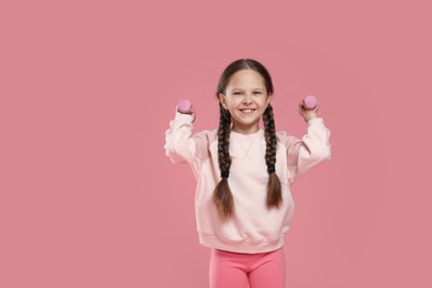 Cute little girl with dumbbells on pink background