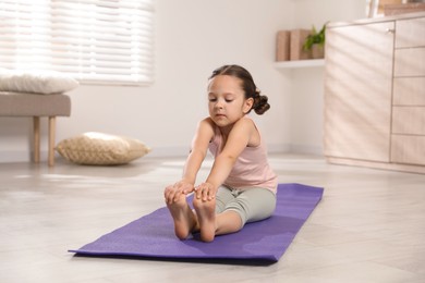 Photo of Cute little girl stretching herself on mat at home