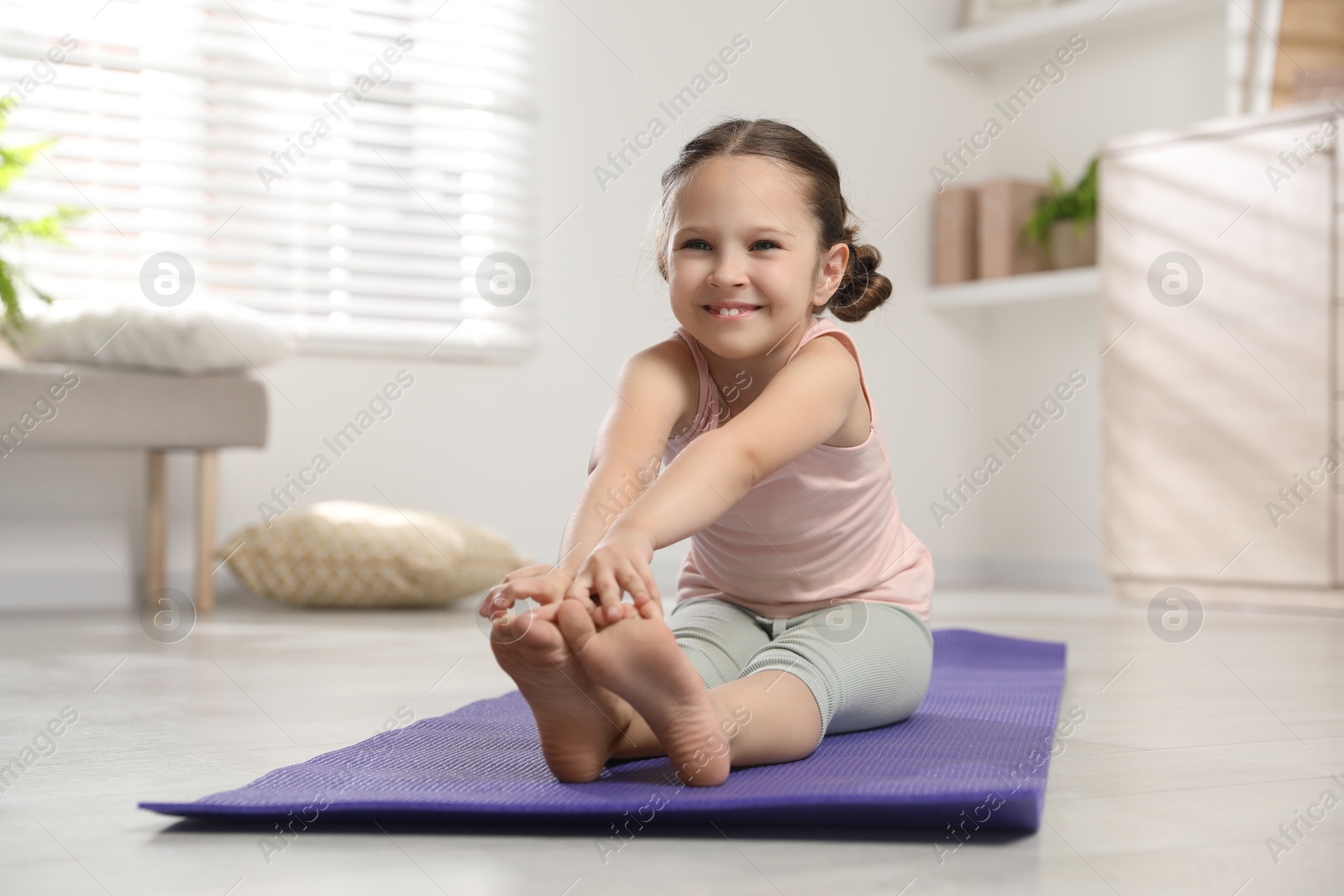 Photo of Cute little girl stretching herself on mat at home