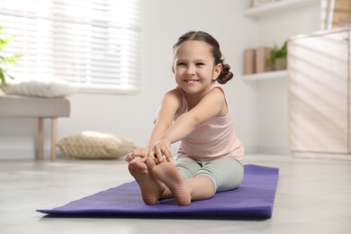 Photo of Cute little girl stretching herself on mat at home