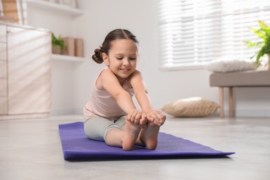 Photo of Cute little girl stretching herself on mat at home