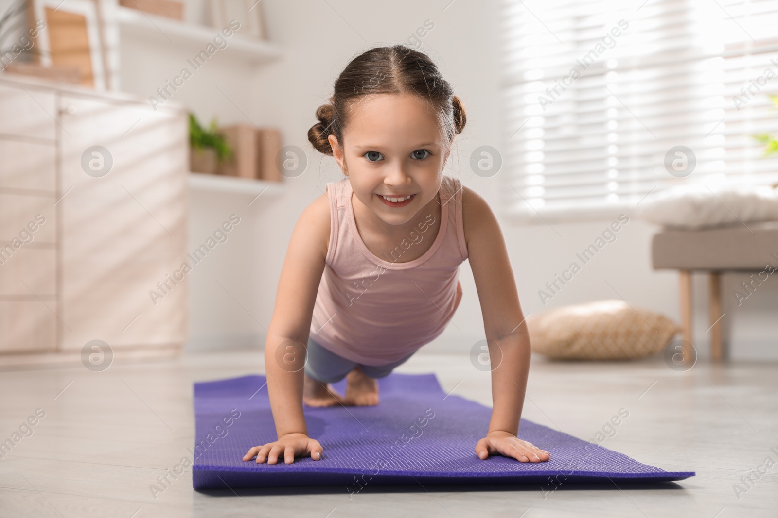 Photo of Cute little girl doing plank exercise at home