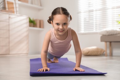 Photo of Cute little girl doing plank exercise at home