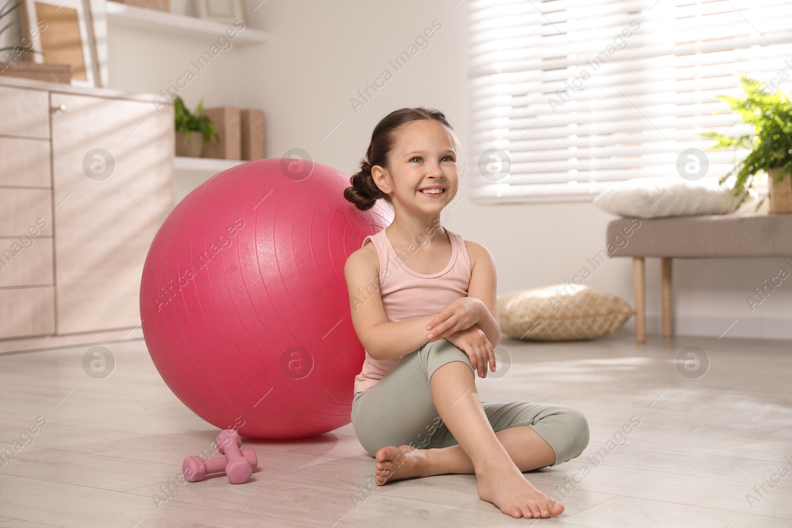 Photo of Cute little girl near dumbbells and fit ball at home