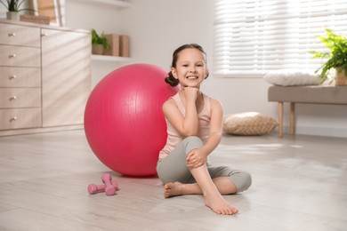 Photo of Cute little girl near dumbbells and fit ball at home