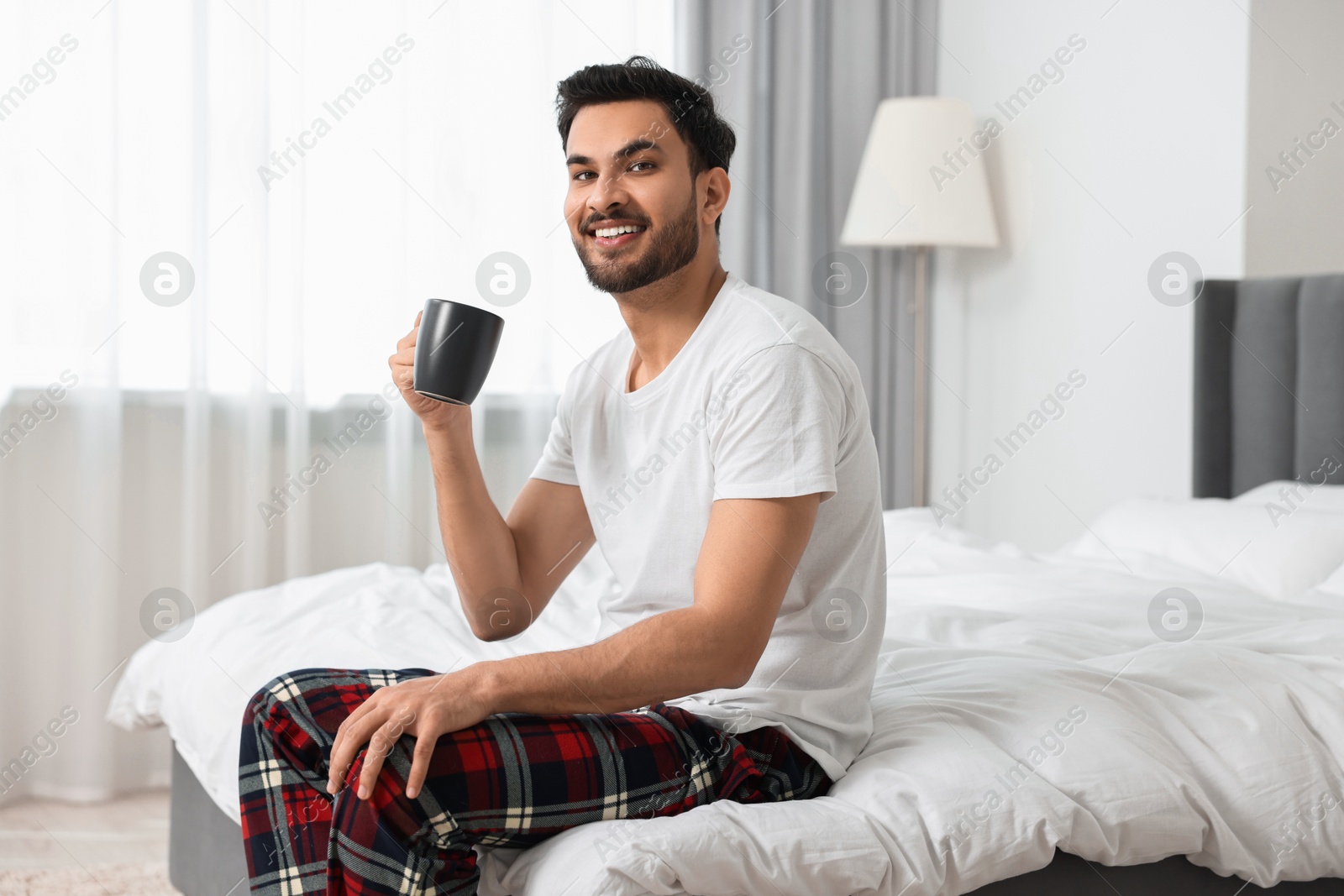 Photo of Happy man with cup of coffee on bed at morning