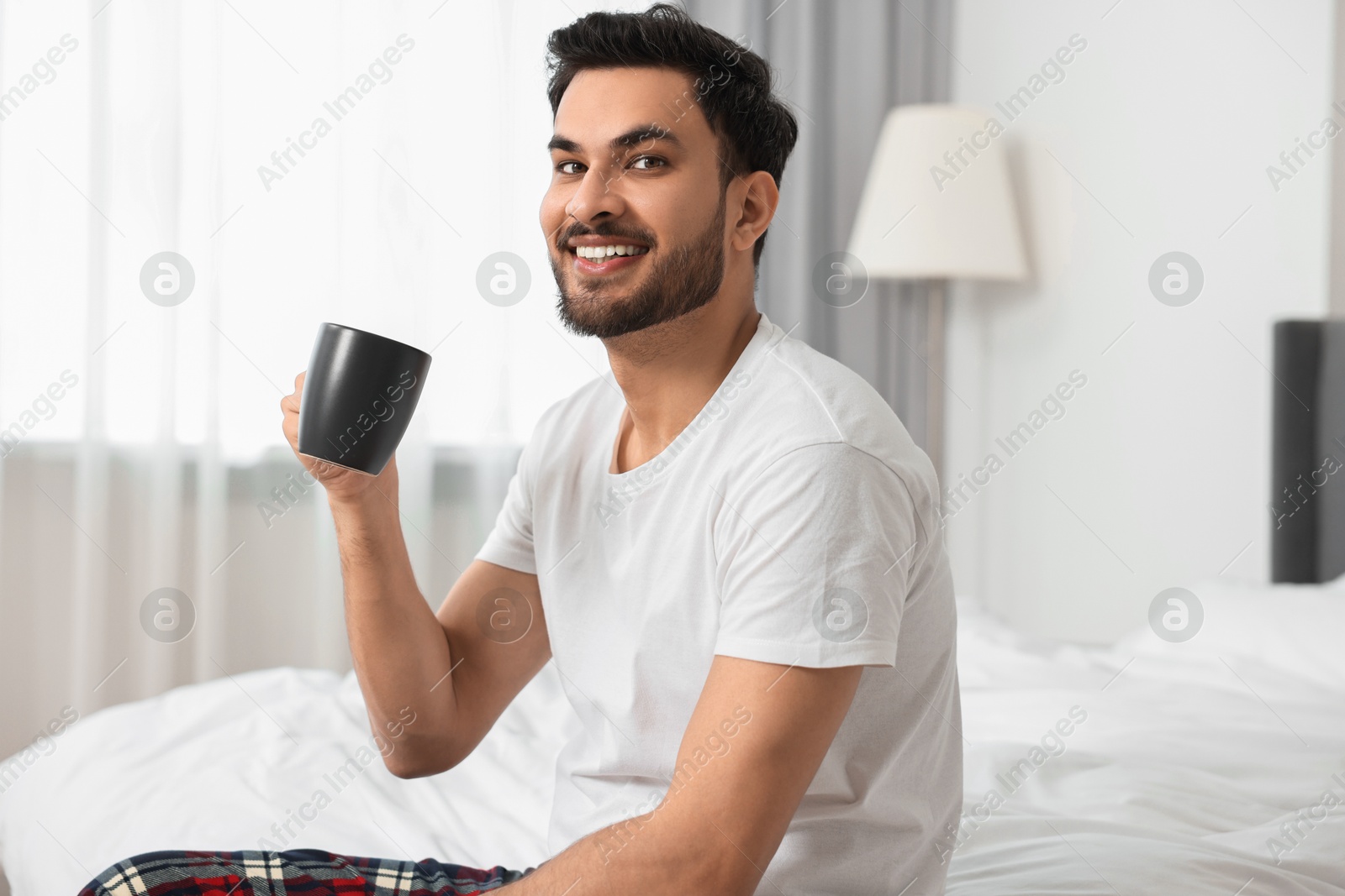 Photo of Happy man with cup of coffee on bed at morning