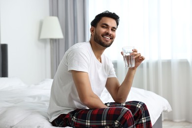 Photo of Happy man with glass of water on bed at morning