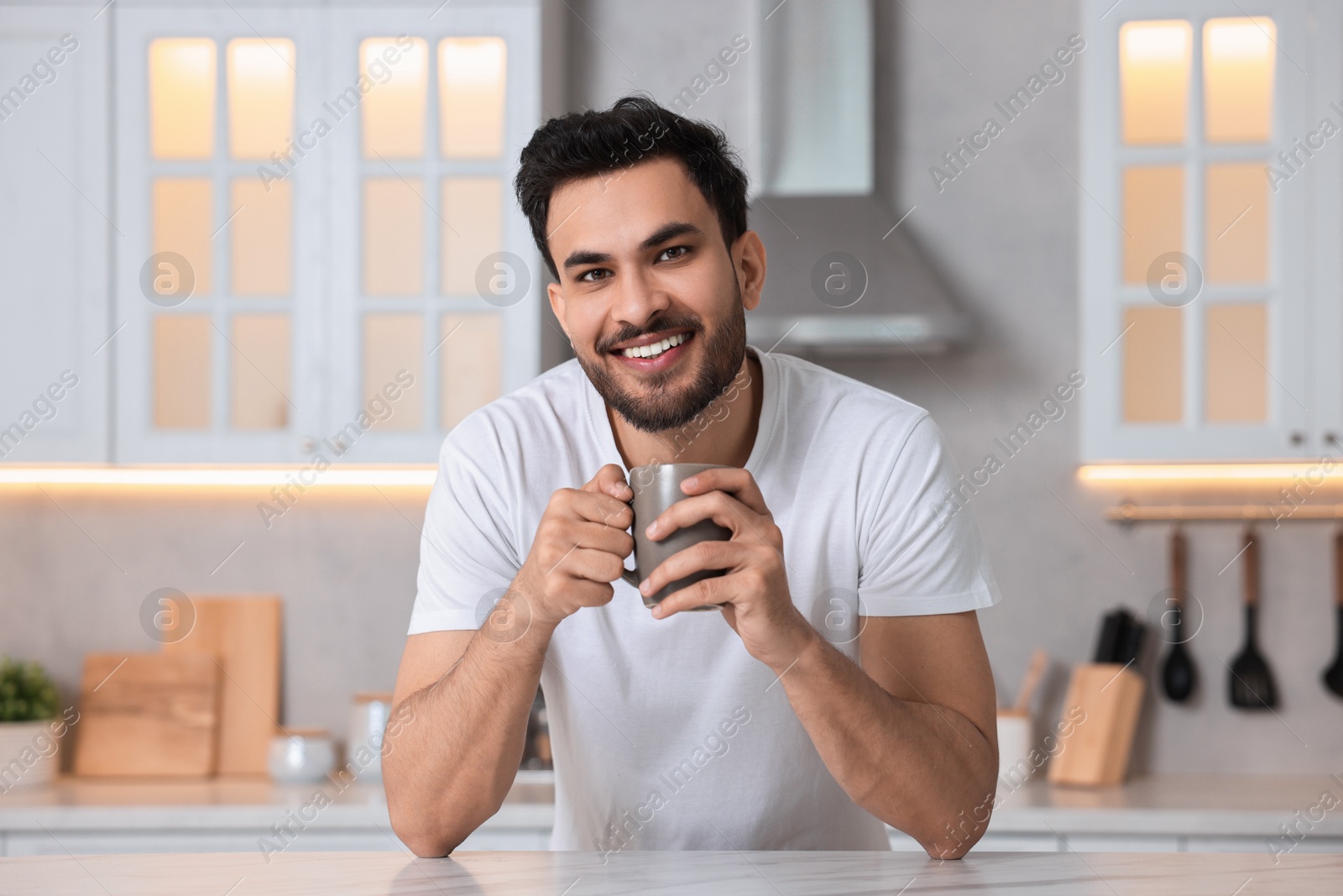 Photo of Morning of happy man with cup of hot drink at table in kitchen