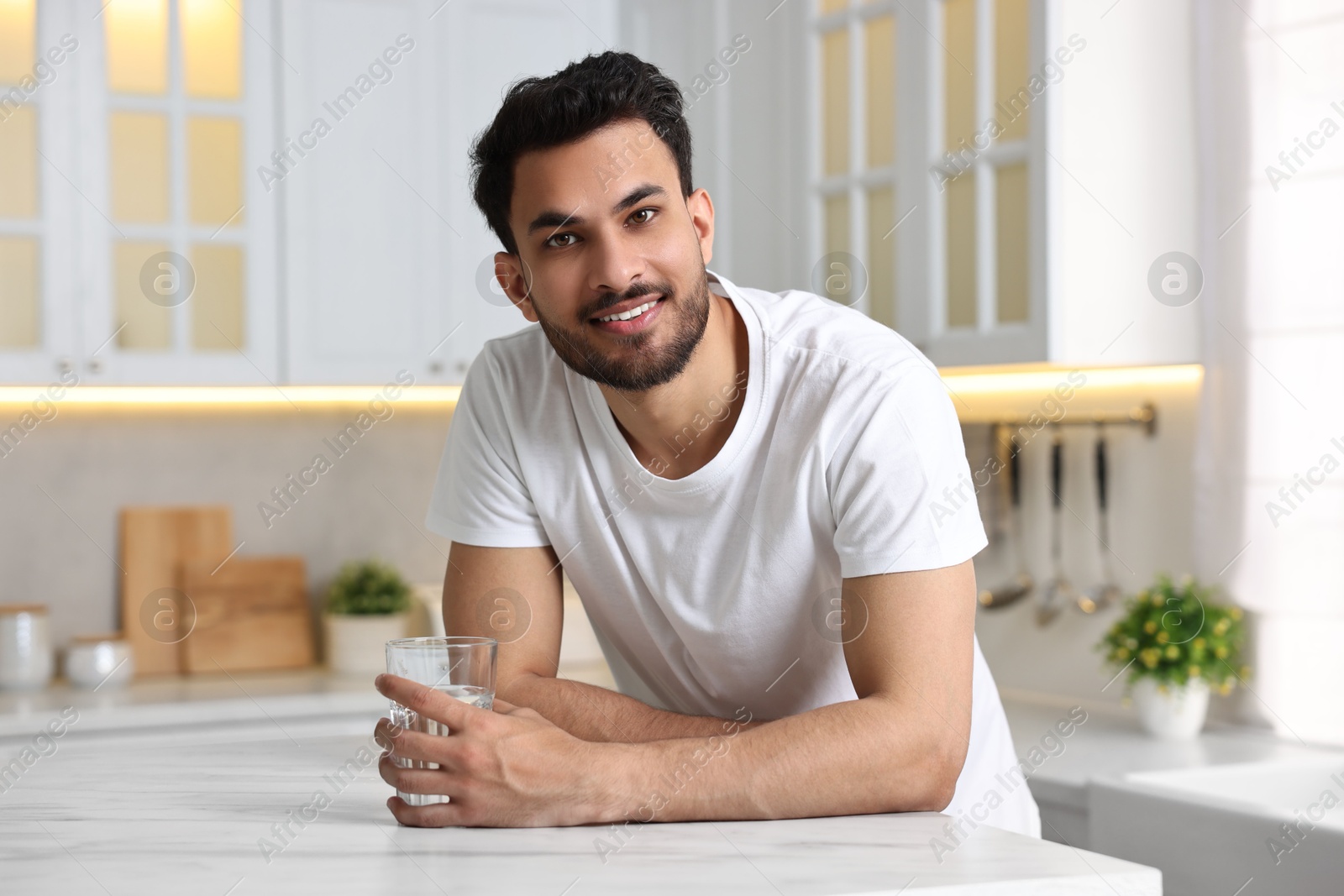 Photo of Happy man with glass of water at table in kitchen at morning