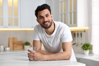 Happy man with glass of water at table in kitchen at morning