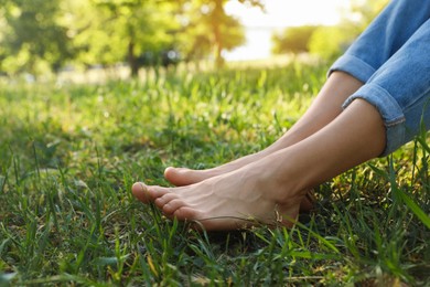 Photo of Woman sitting barefoot on green grass outdoors, closeup. Space for text