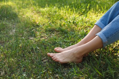 Photo of Woman sitting barefoot on green grass outdoors, closeup. Space for text